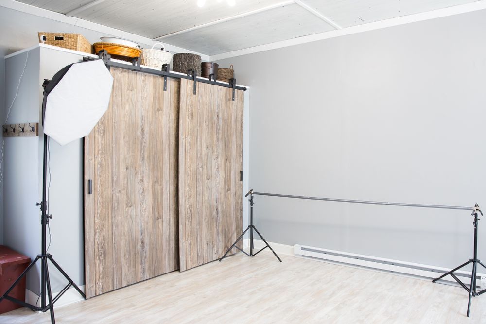 Professional photography studio setup with wooden backdrop and lighting equipment on light hardwood flooring.