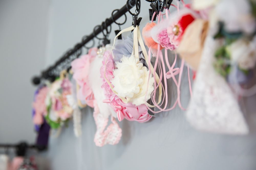 Delicate pink and white floral arrangements hang from a black rack against a gray background.