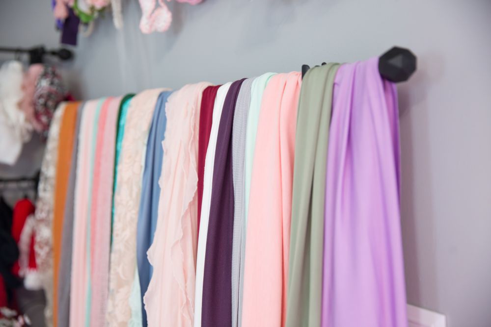 Colorful fabric backdrops in pastel shades hanging neatly on a black curtain rod against a gray wall.