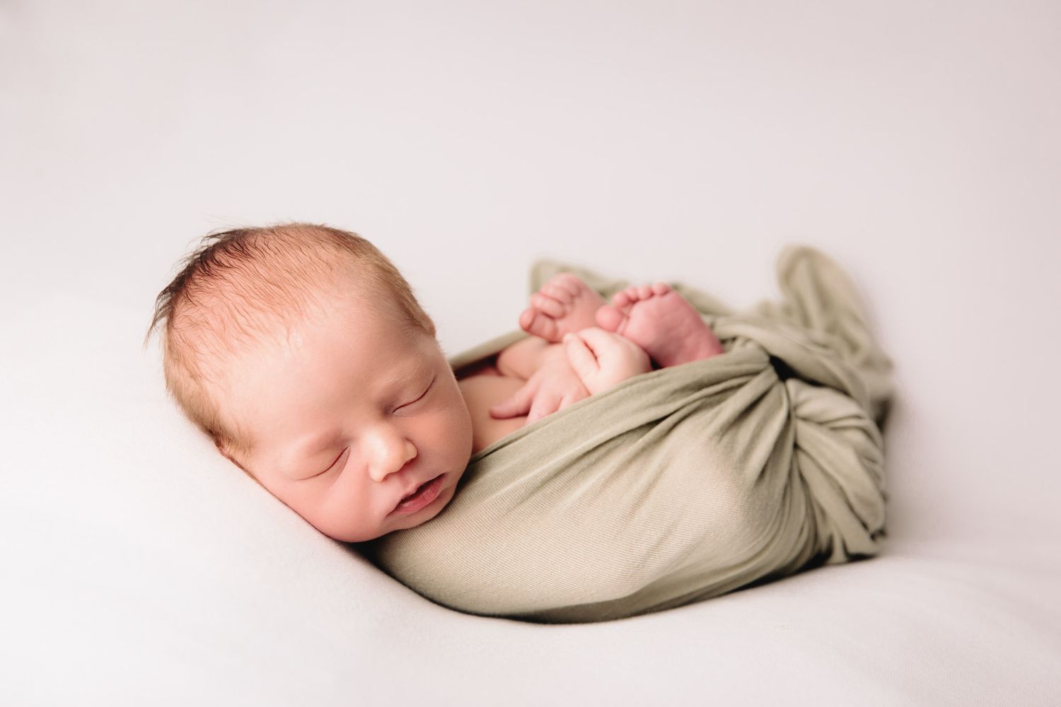 baby boy wrapped in sage green on white blanket