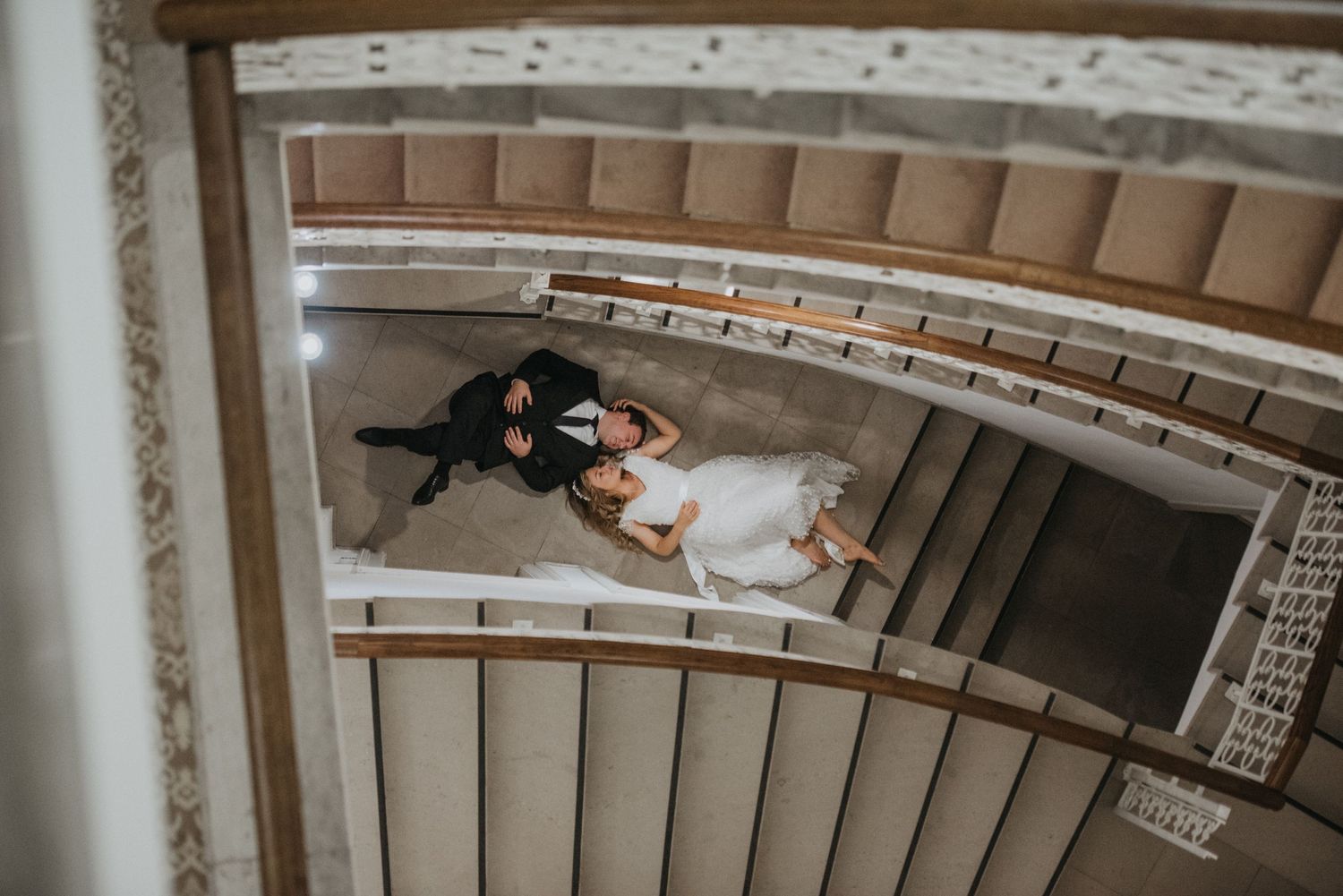 A spiral staircase view of a romantic wedding couple embracing from above.