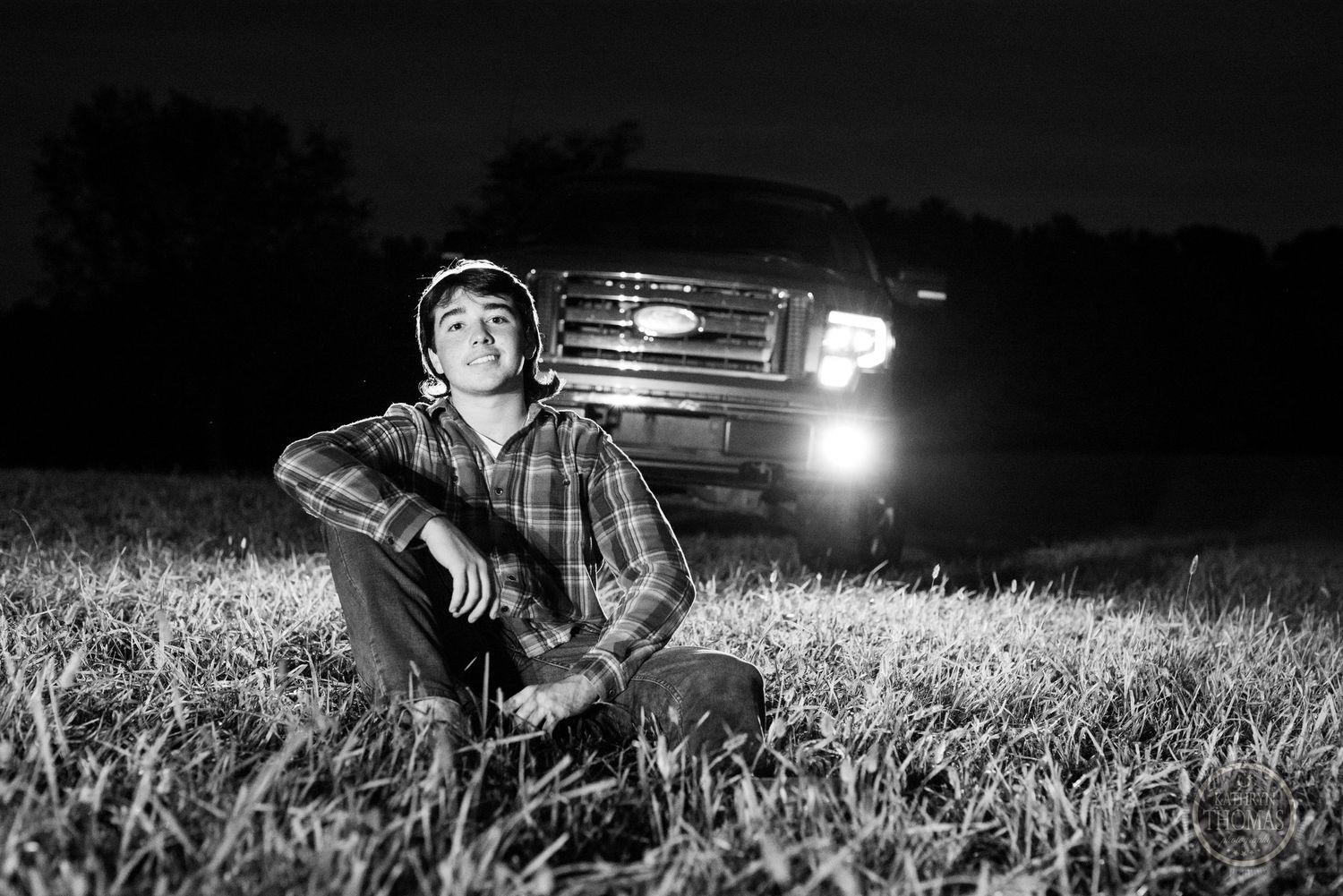 Black and white portrait with truck headlights illuminating a grassy field at night.