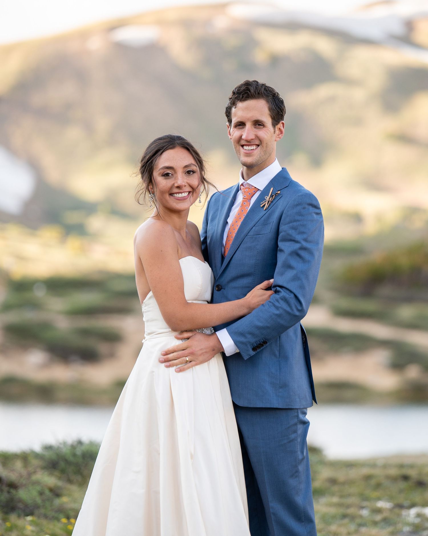 A joyful wedding couple poses against a mountainous backdrop at sunset.