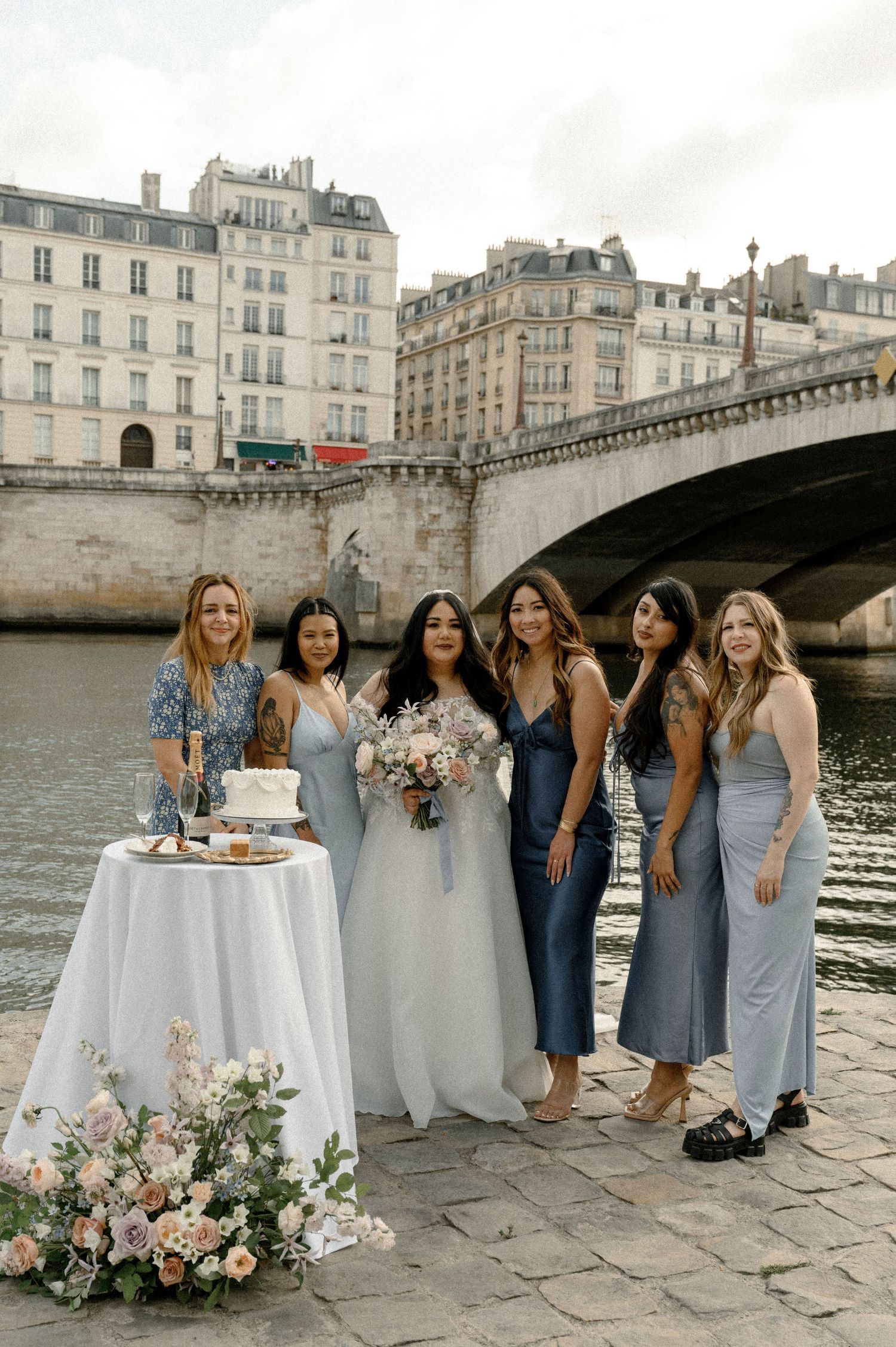 Bridal party posing by the Seine River in Paris with elegant table setup and floral arrangements.