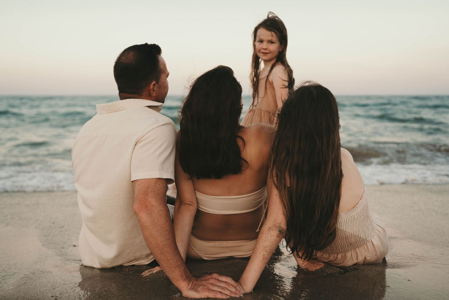Group sitting together watching sunset on beach with ocean waves in background.