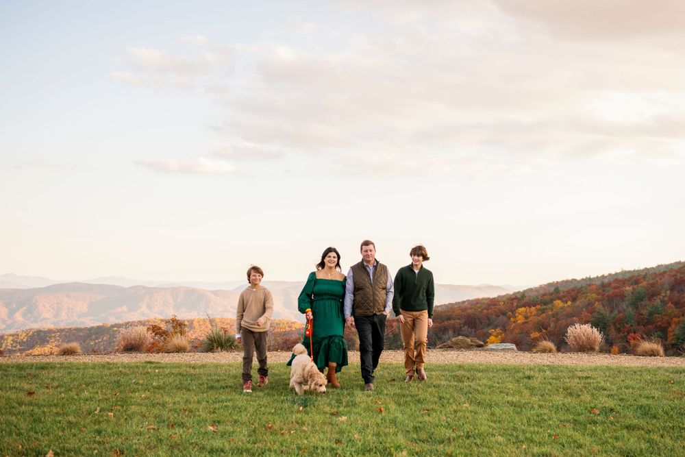 A group walks together with their dog across a hilltop meadow during golden hour with mountains in the background.