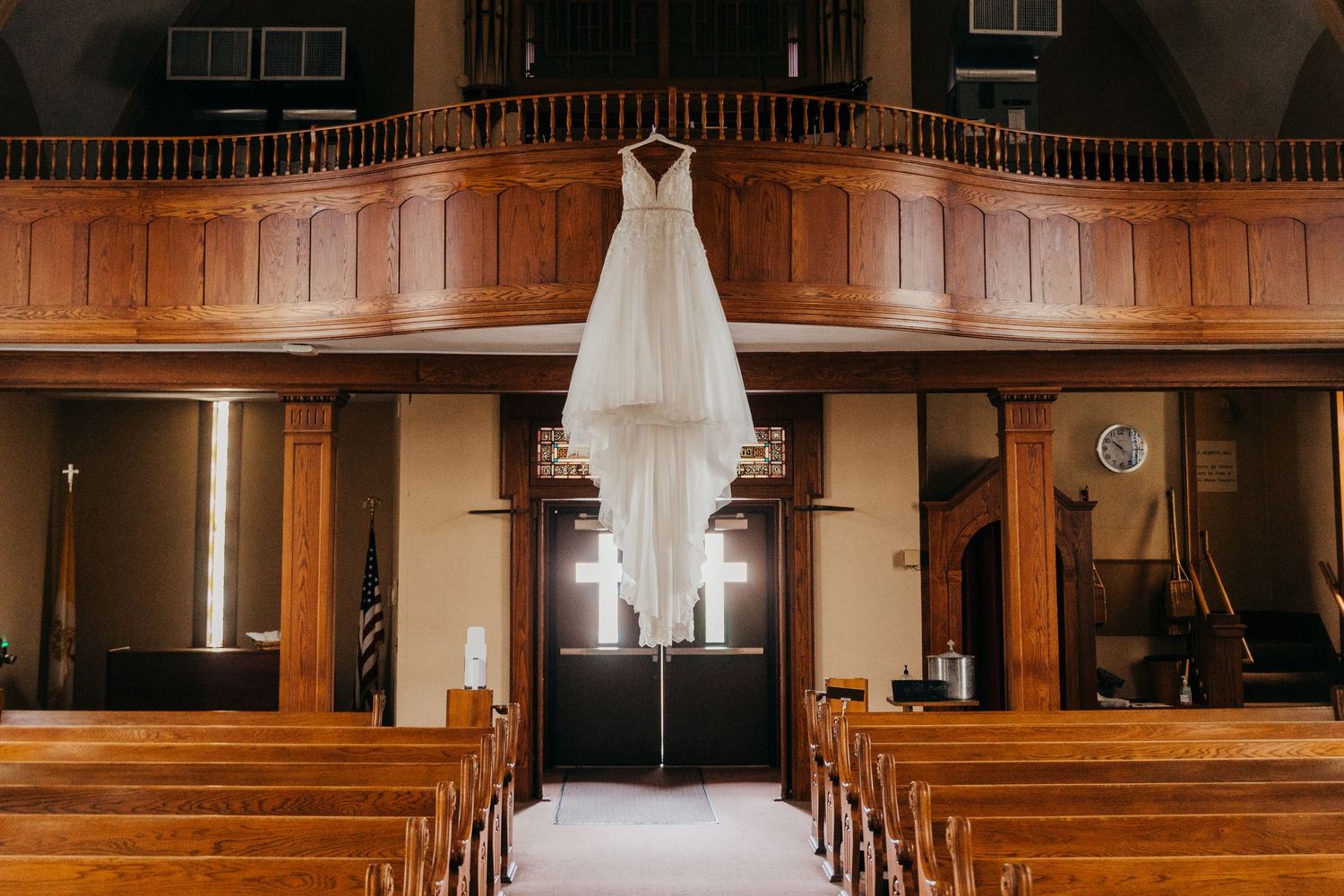 A wedding dress hangs elegantly in a wooden church sanctuary with pews.