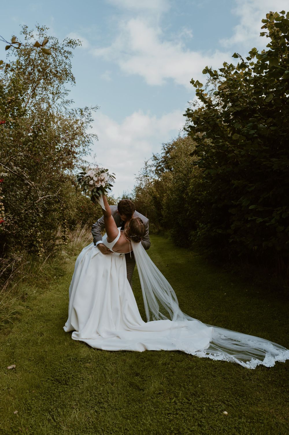 Groom dipping the bride into a kiss with the bouquet in the air at Hareston Manor