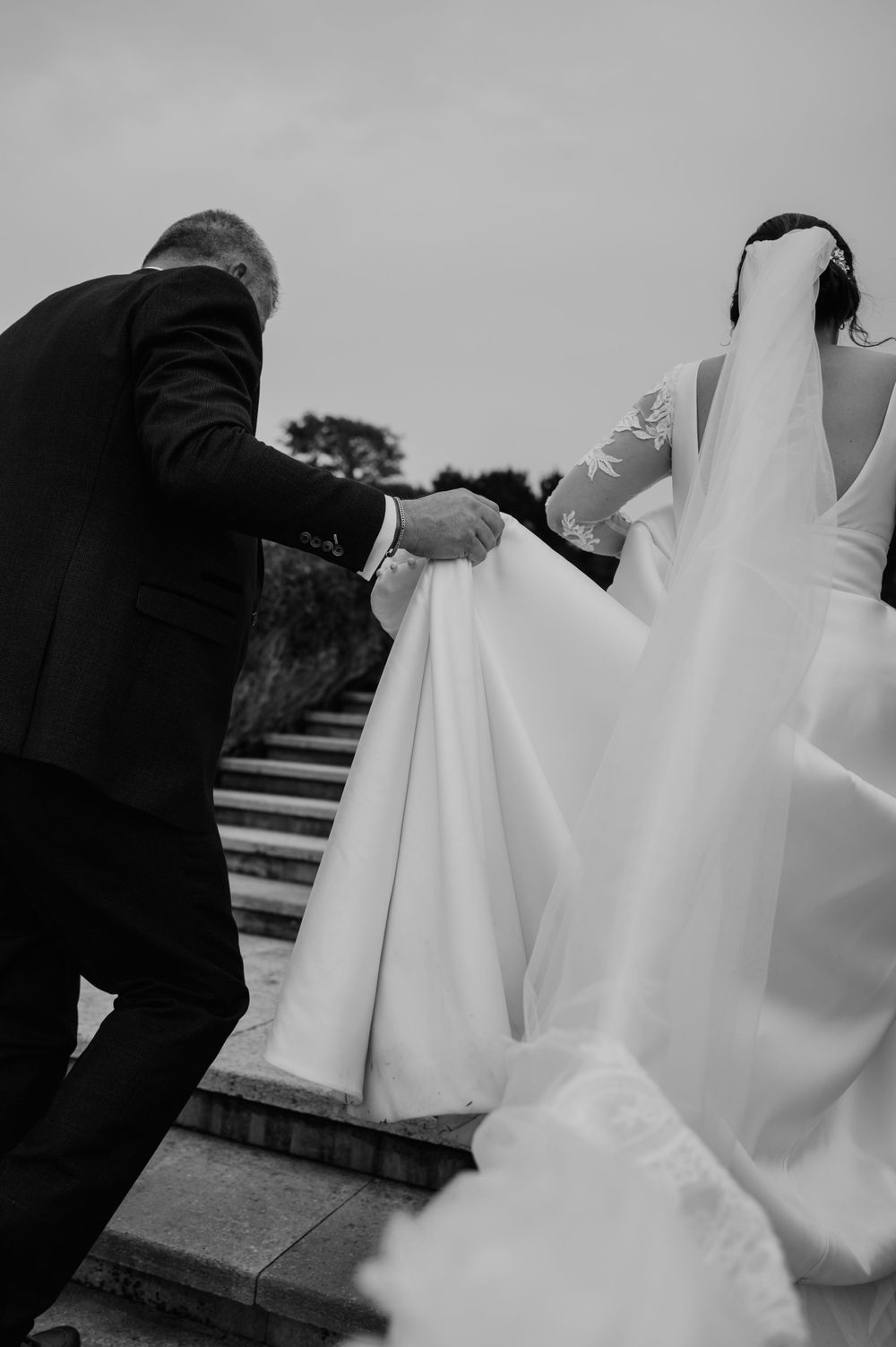 Groom holding the brides dress as they walk up the stairs at Tregenna Castle
