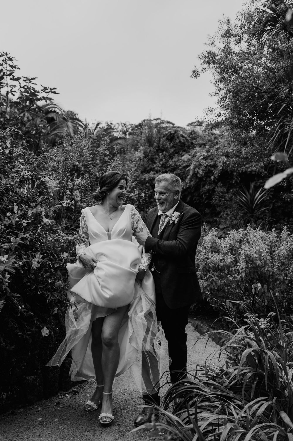 Bride and groom walking as the bride hoists her dress up and the groom helps at Tregenna Castle