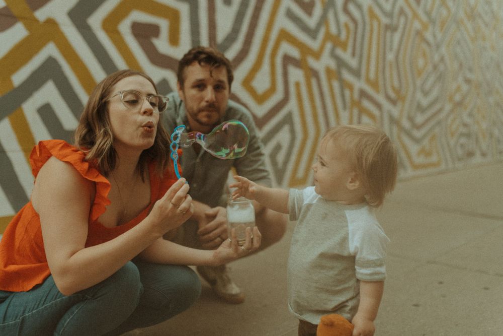 Family blowing bubbles together in front of an artistic wall mural.