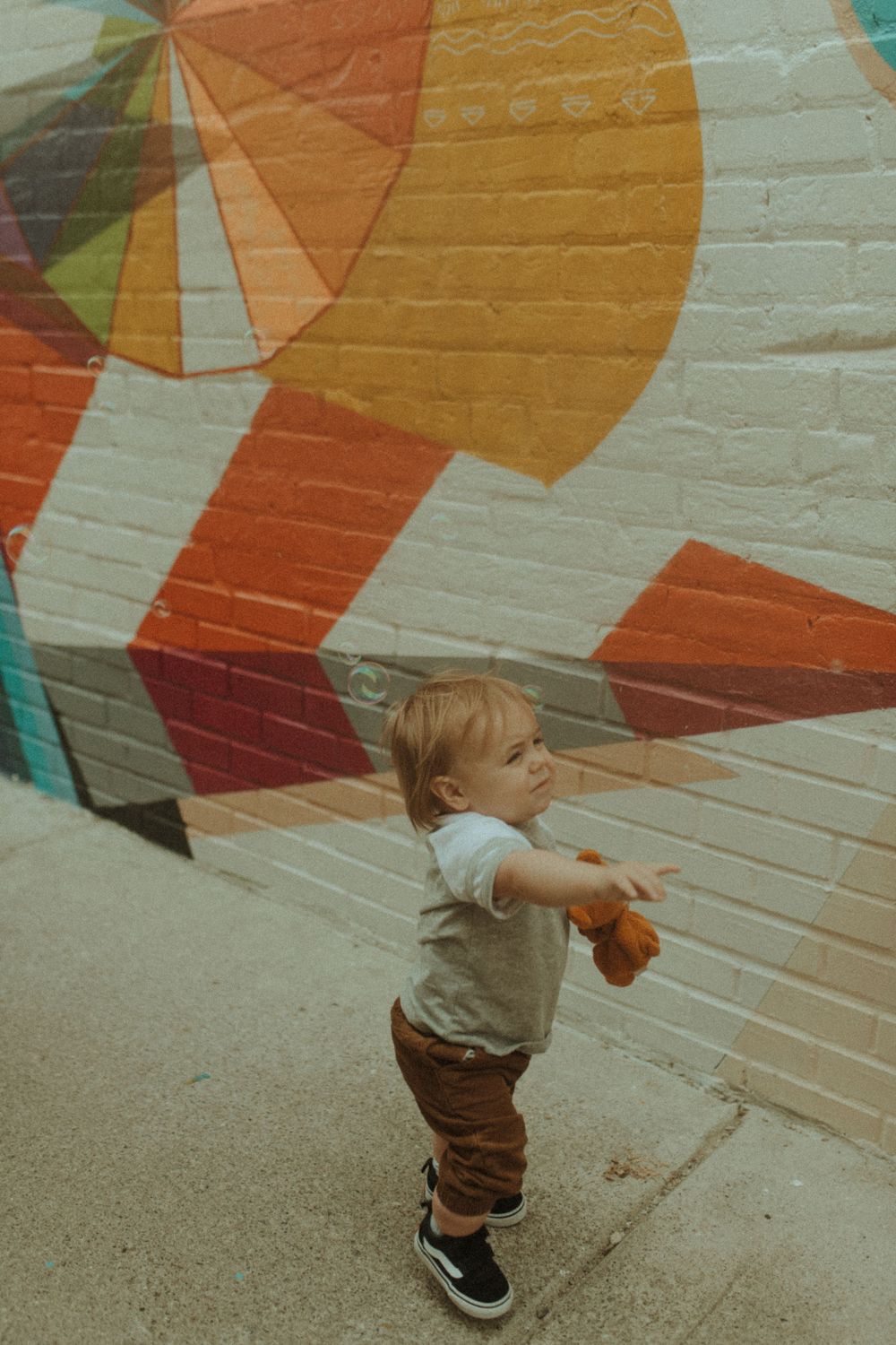Toddler in grey shirt exploring near colorful geometric wall art.