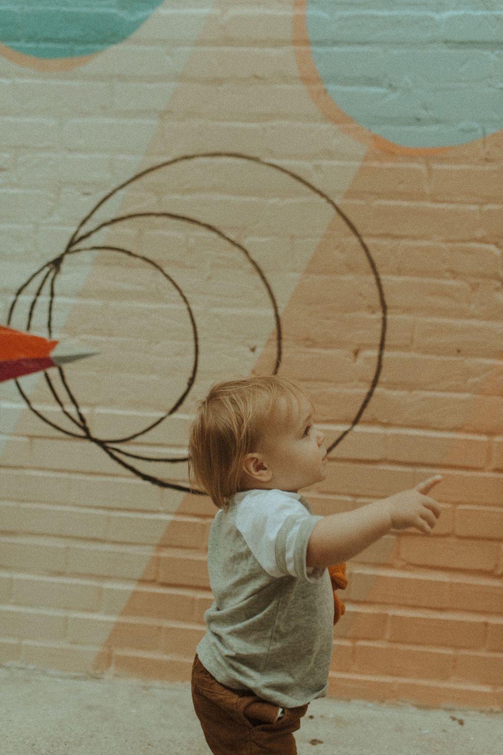 Toddler reaching up towards circular patterns on a painted wall.