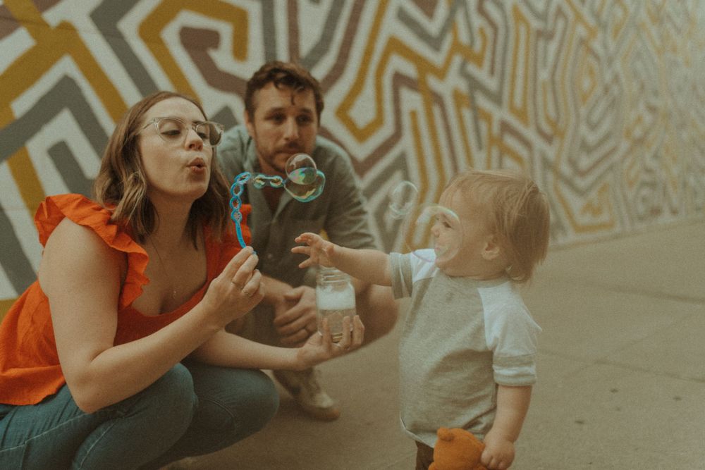 A family blowing bubbles together against a geometric wall mural.