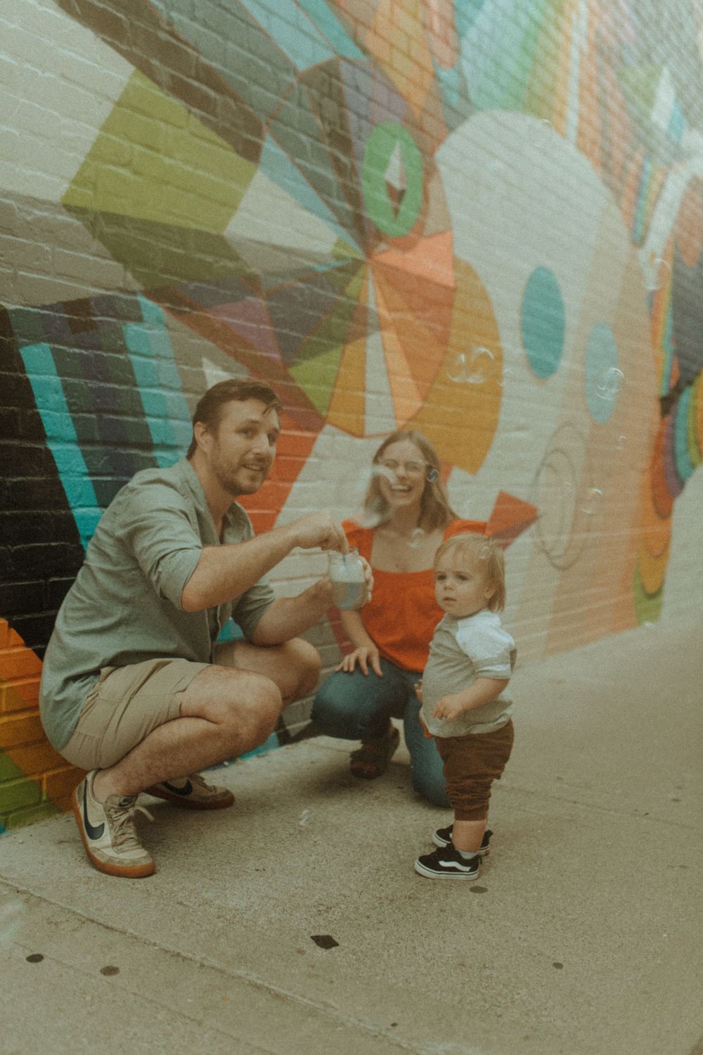 A family shares a playful moment against a colorful geometric mural wall.