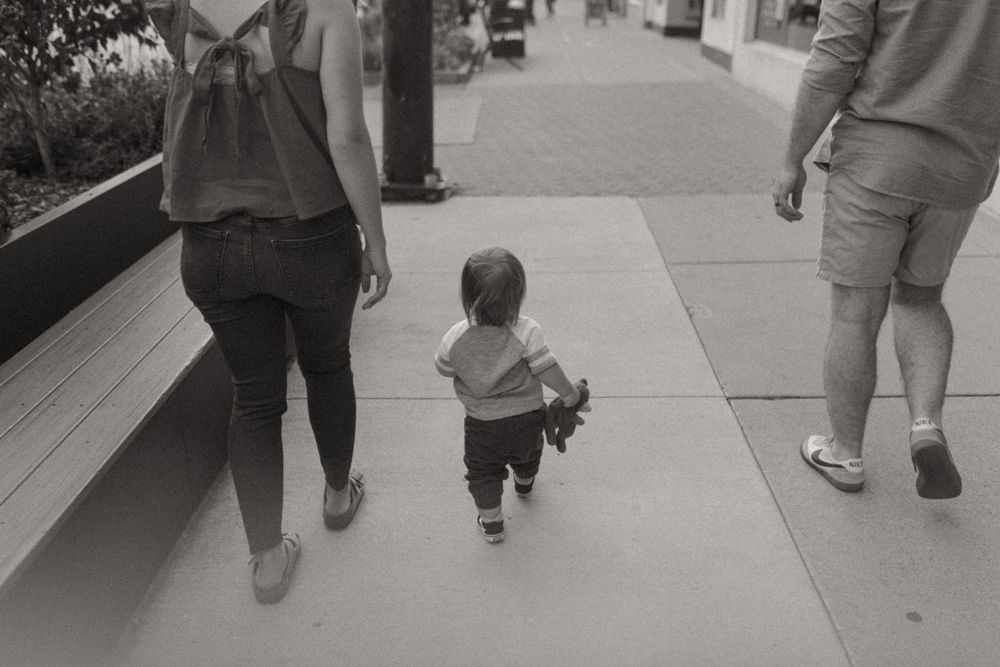 Toddler walking between adults on modern urban pathway.