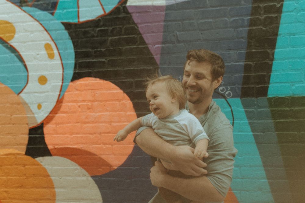 Playful moment captured in front of vibrant street art mural with bright colors.