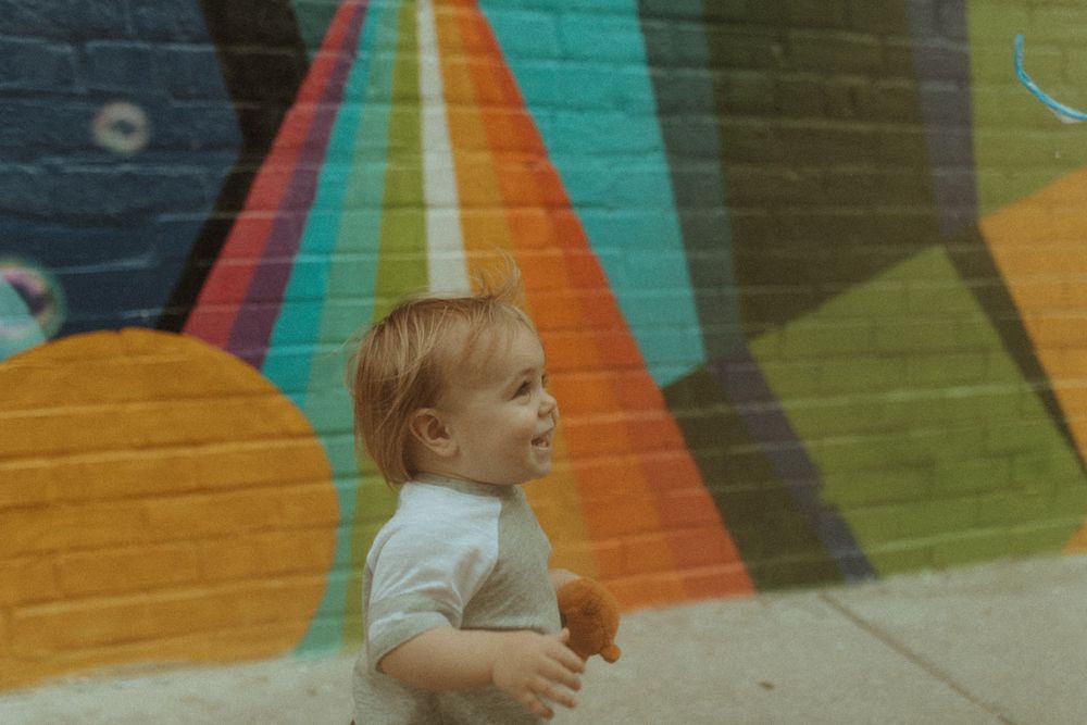 Small toddler explores near vibrant street art with geometric patterns.