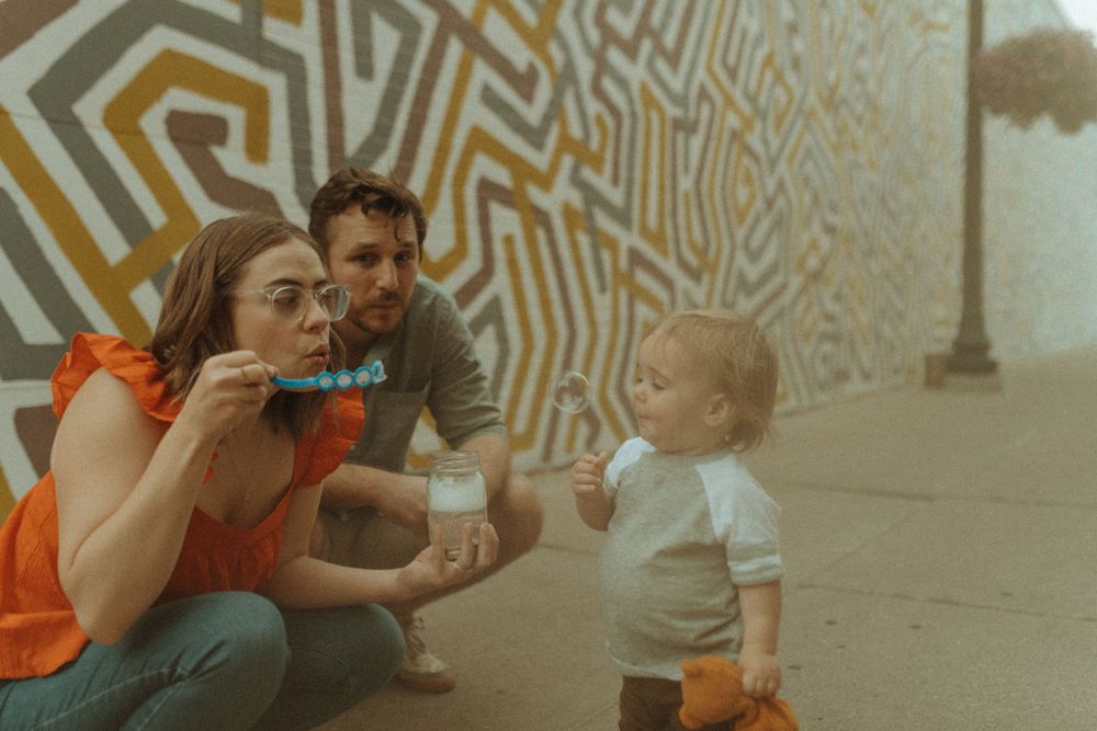 Family blowing bubbles together against geometric wall art.