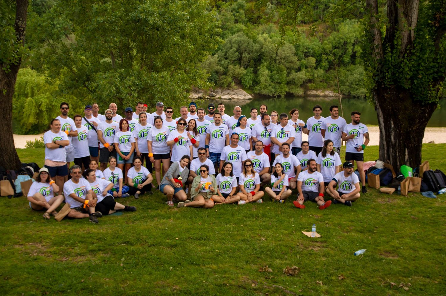 Large group photo of people wearing matching white shirts sitting outdoors on grass.