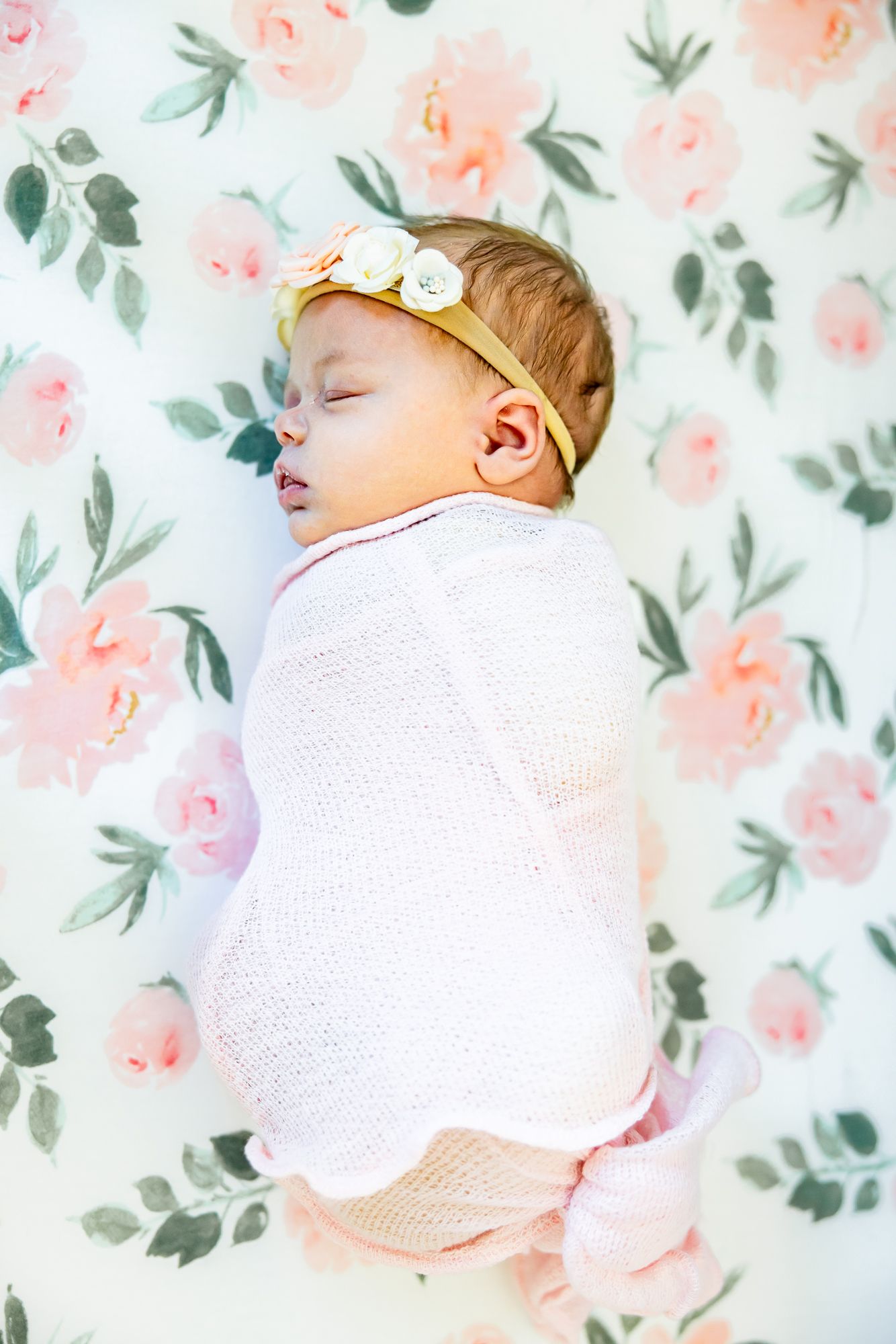 Baby girl sleeps in a pink swaddle on her flowery sheet during newborn photos in Colorado Springs.
