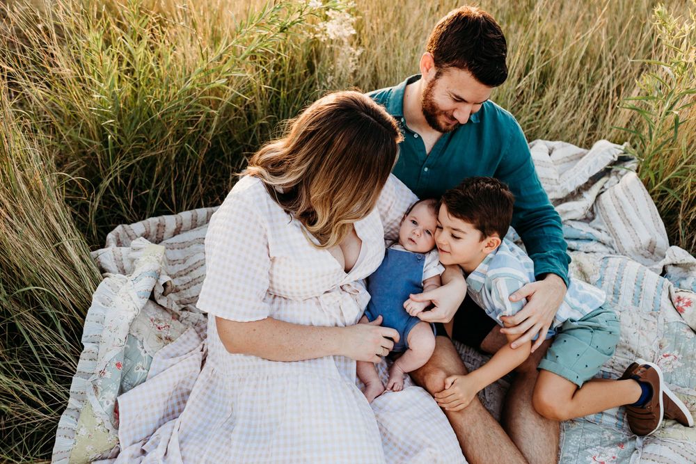 A family shares an intimate moment on a picnic blanket in tall grass.