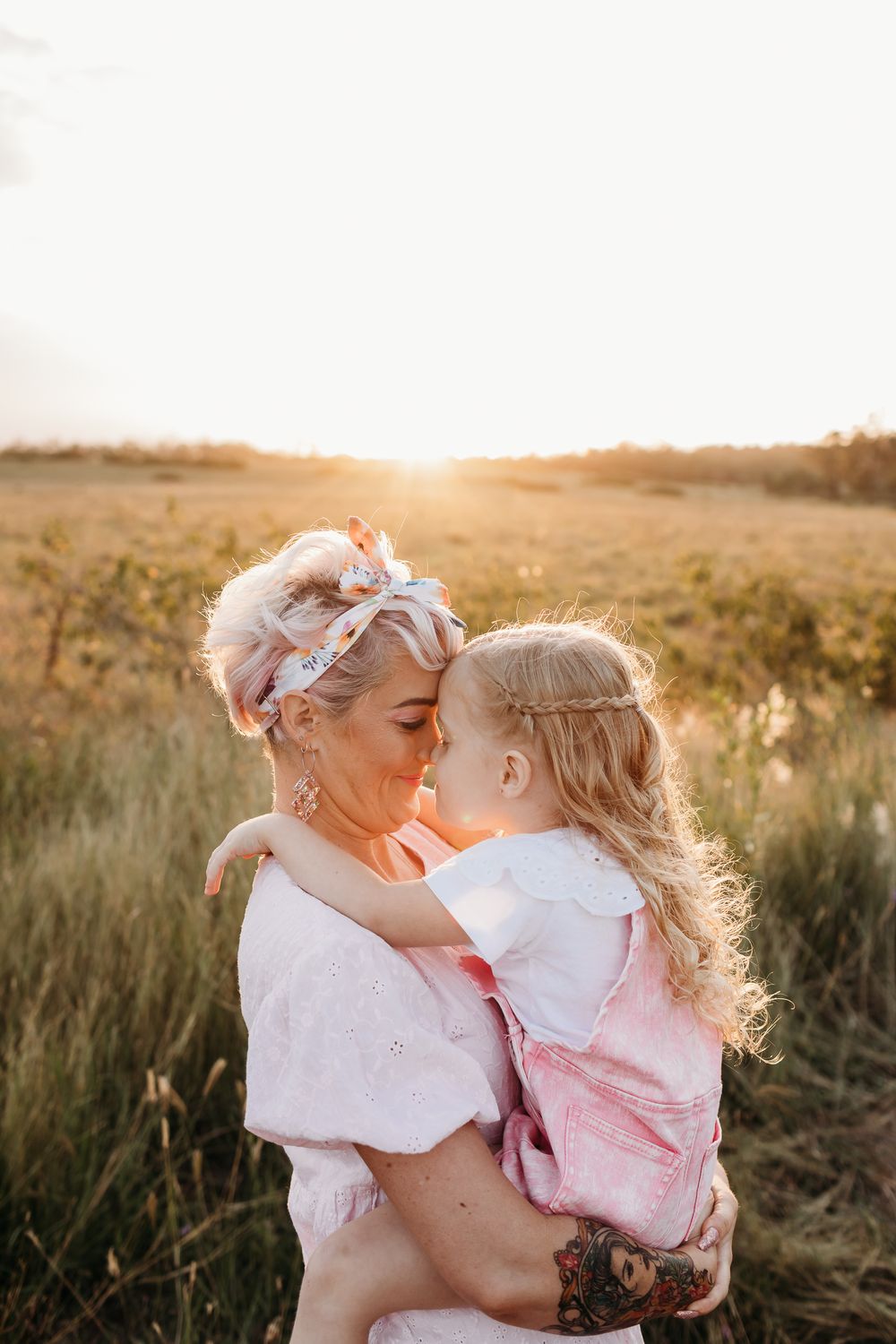 Sweet maternal moments photographed against a warm sunset backdrop in a field.