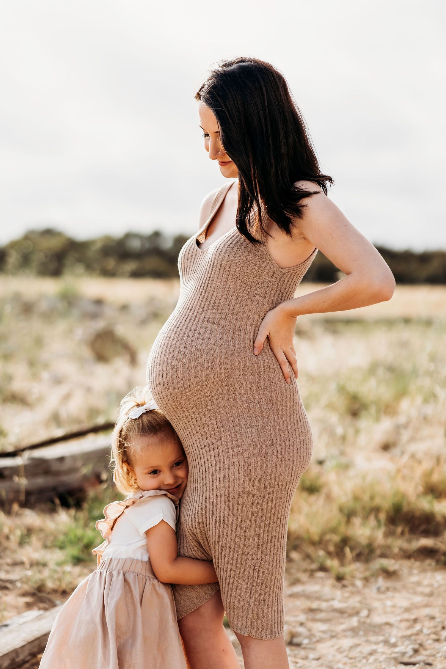 Intimate maternity moment with young child hugging pregnant belly in outdoor setting.