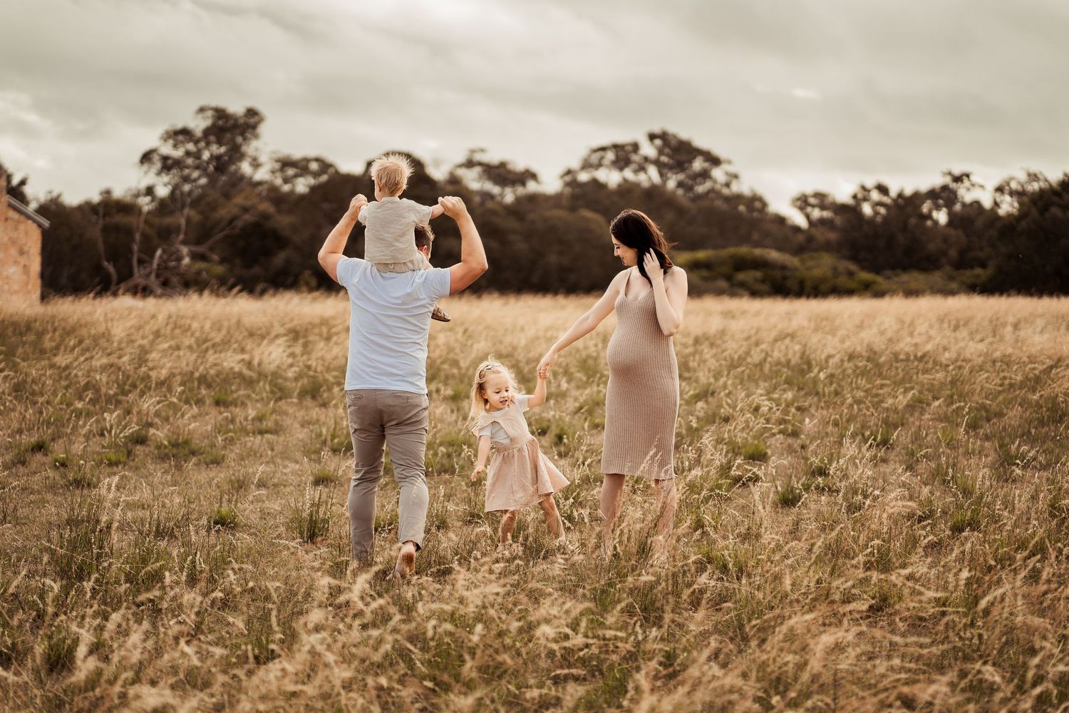Family enjoying playful moments in a sunlit meadow with dramatic clouds overhead.