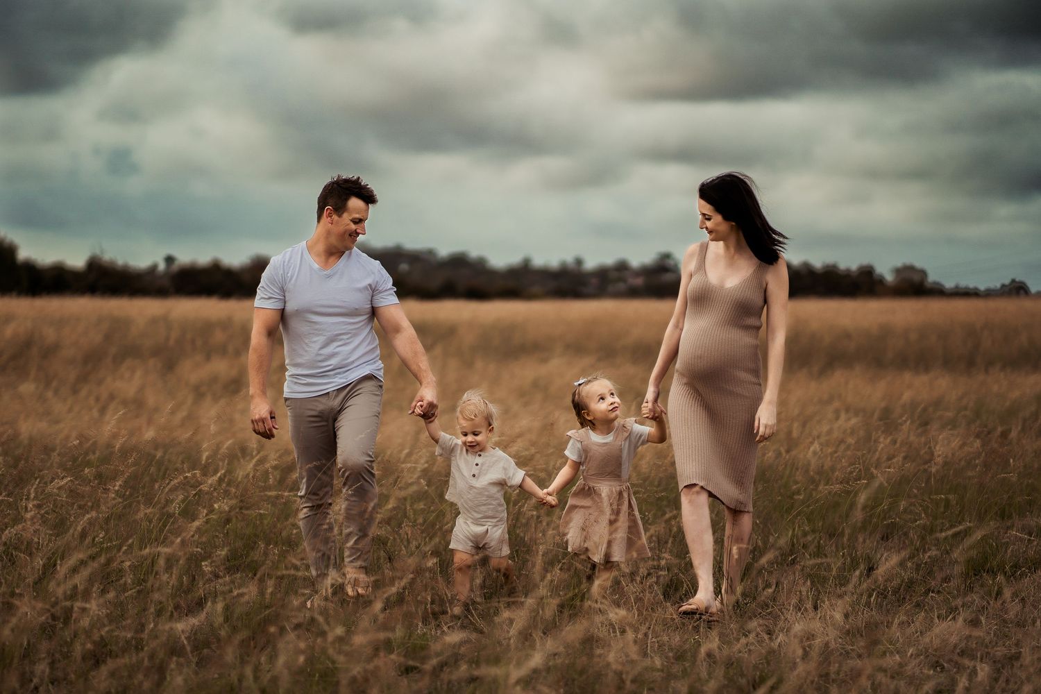 Family of four walking together hand in hand through a scenic autumn field.