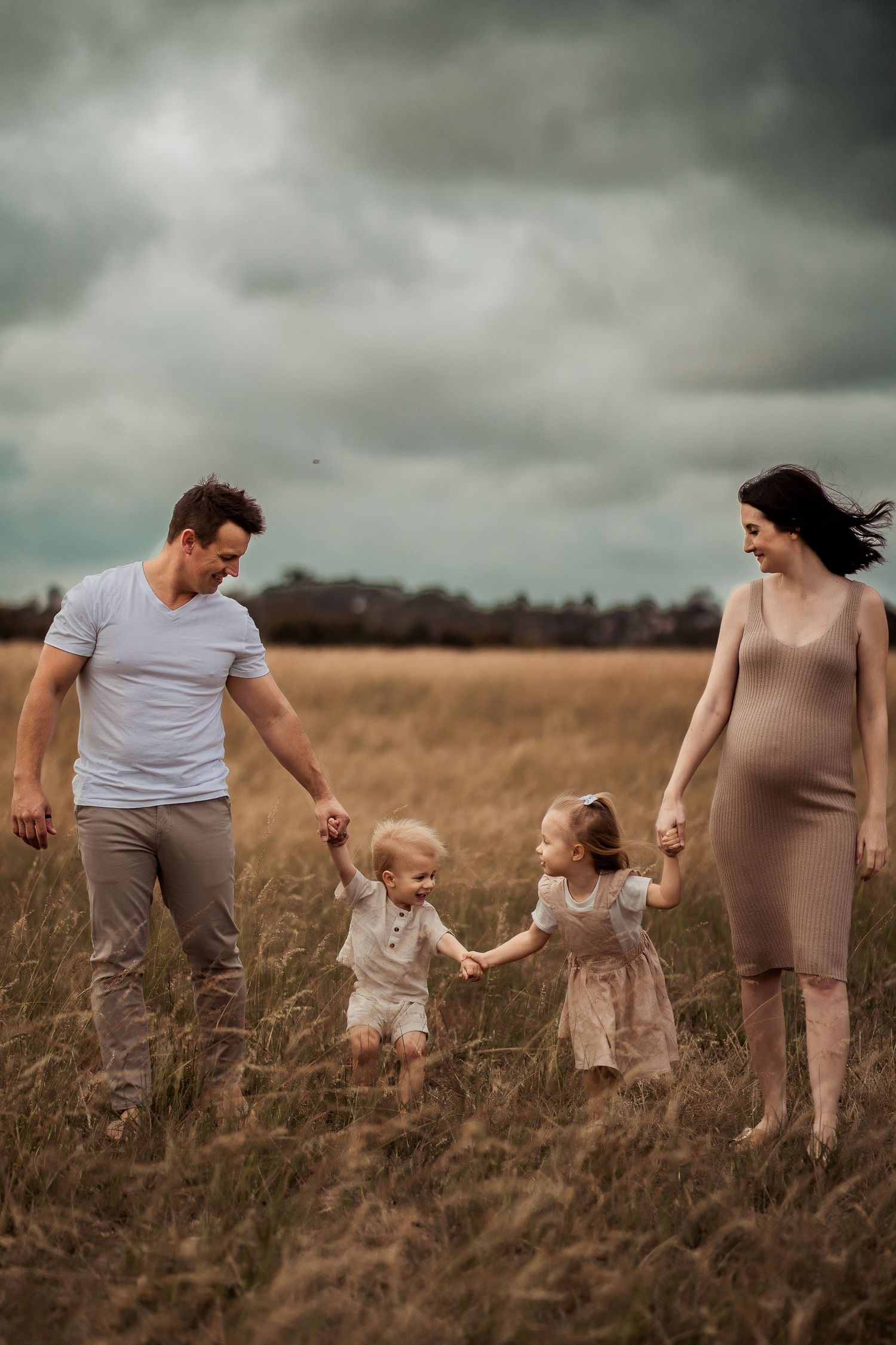 Family holding hands and walking through tall grass in a moody outdoor setting.