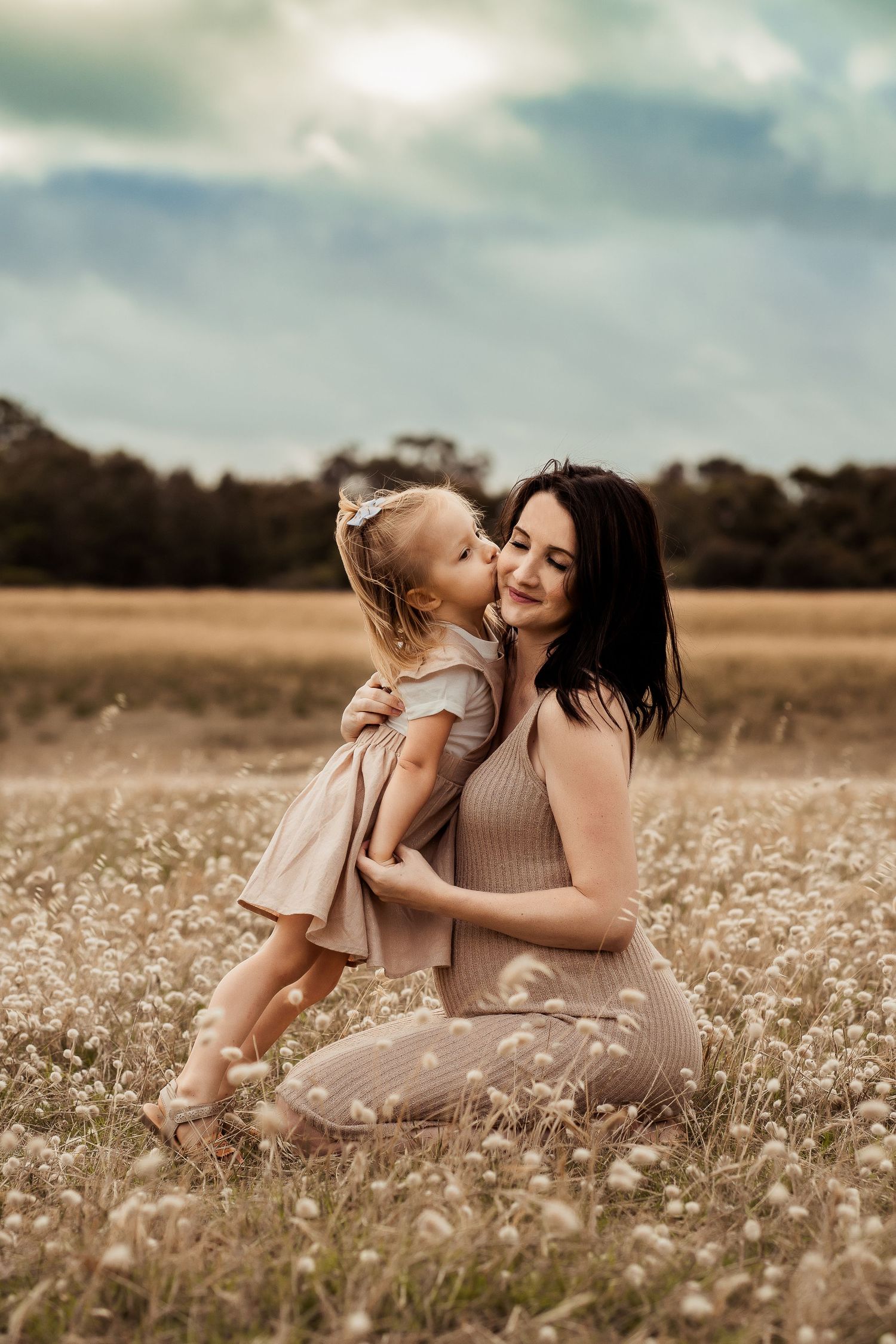A tender moment between mother and daughter in a golden field of wildflowers at sunset.