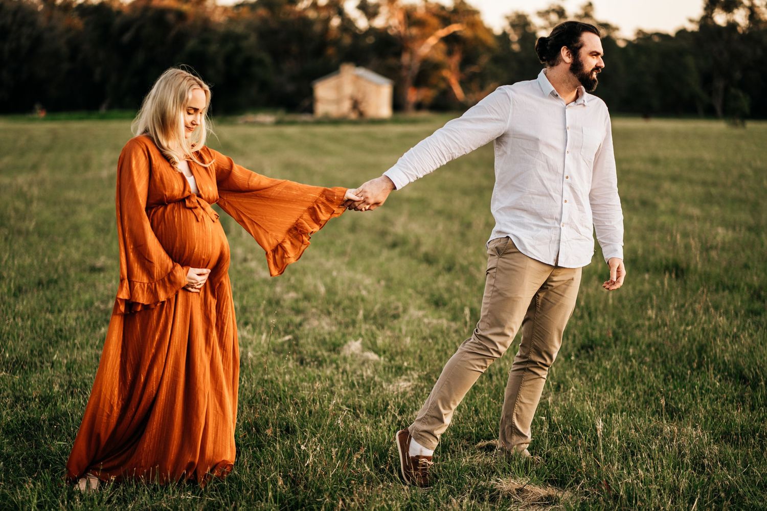 A playful maternity photo in a grassy field at golden hour.