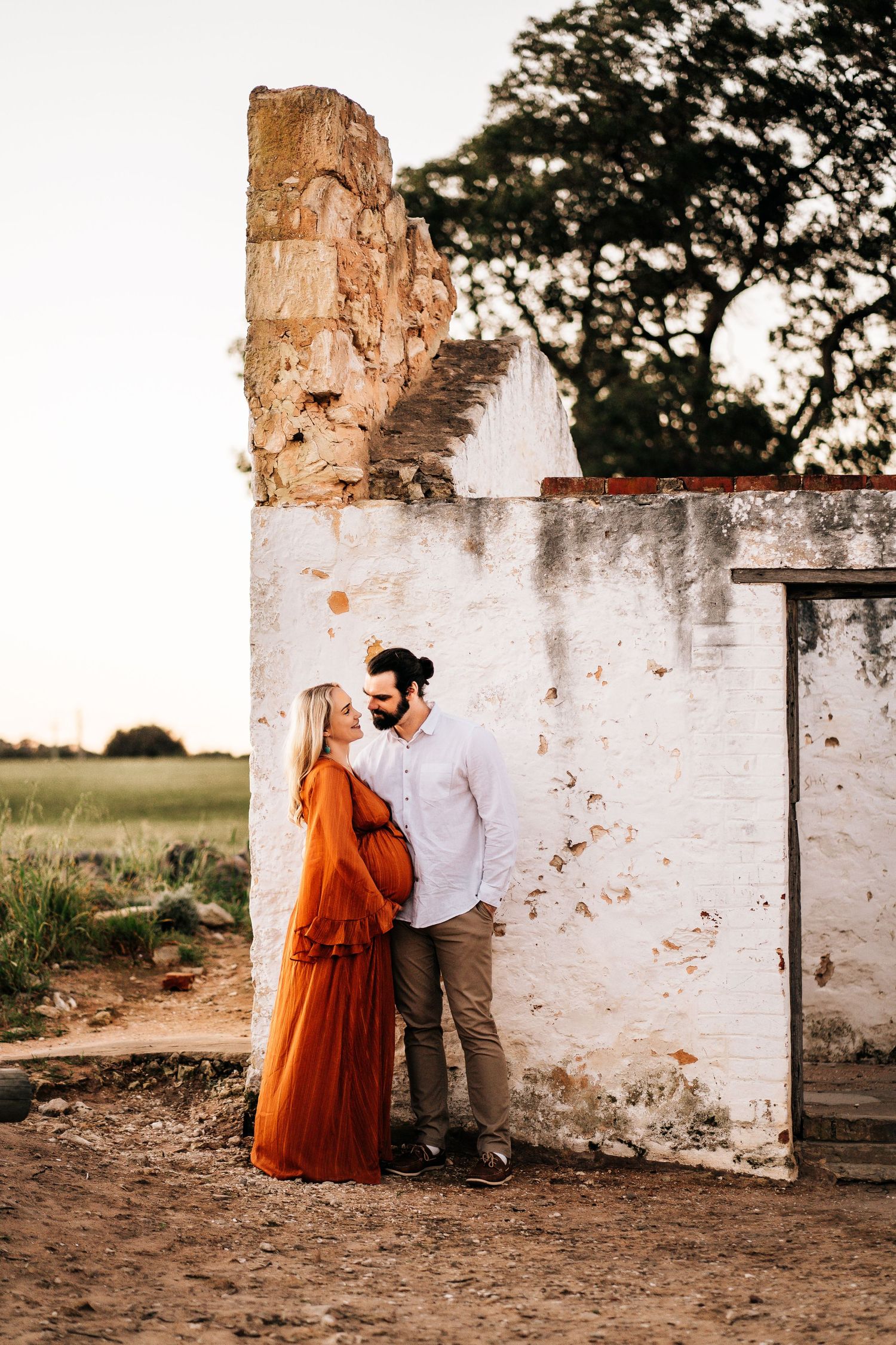 A romantic moment captured against a weathered white wall at sunset.