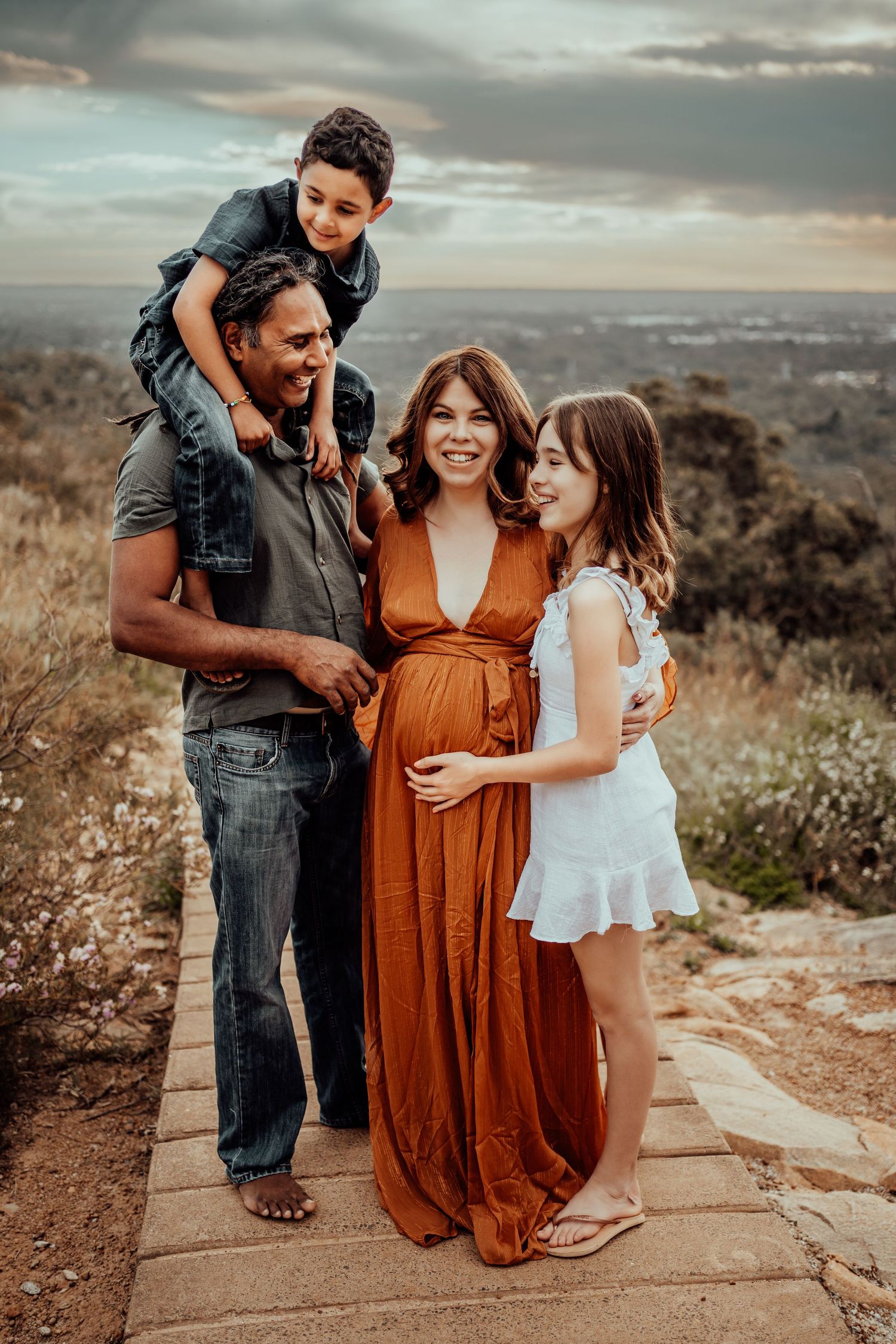 Family portrait on mountain path with city views during sunset maternity session.