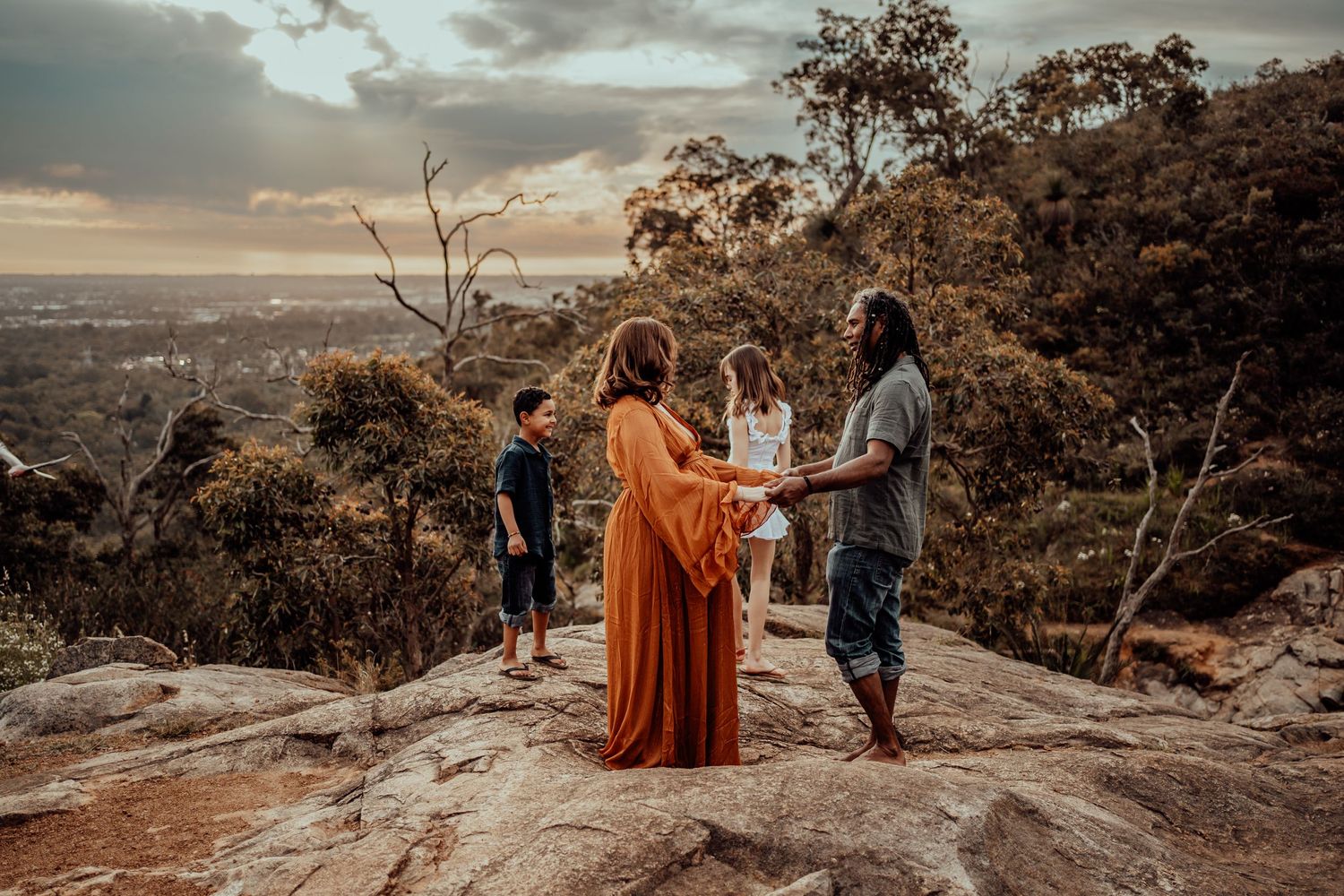 Family gathered on mountain overlook during sunset maternity photoshoot.
