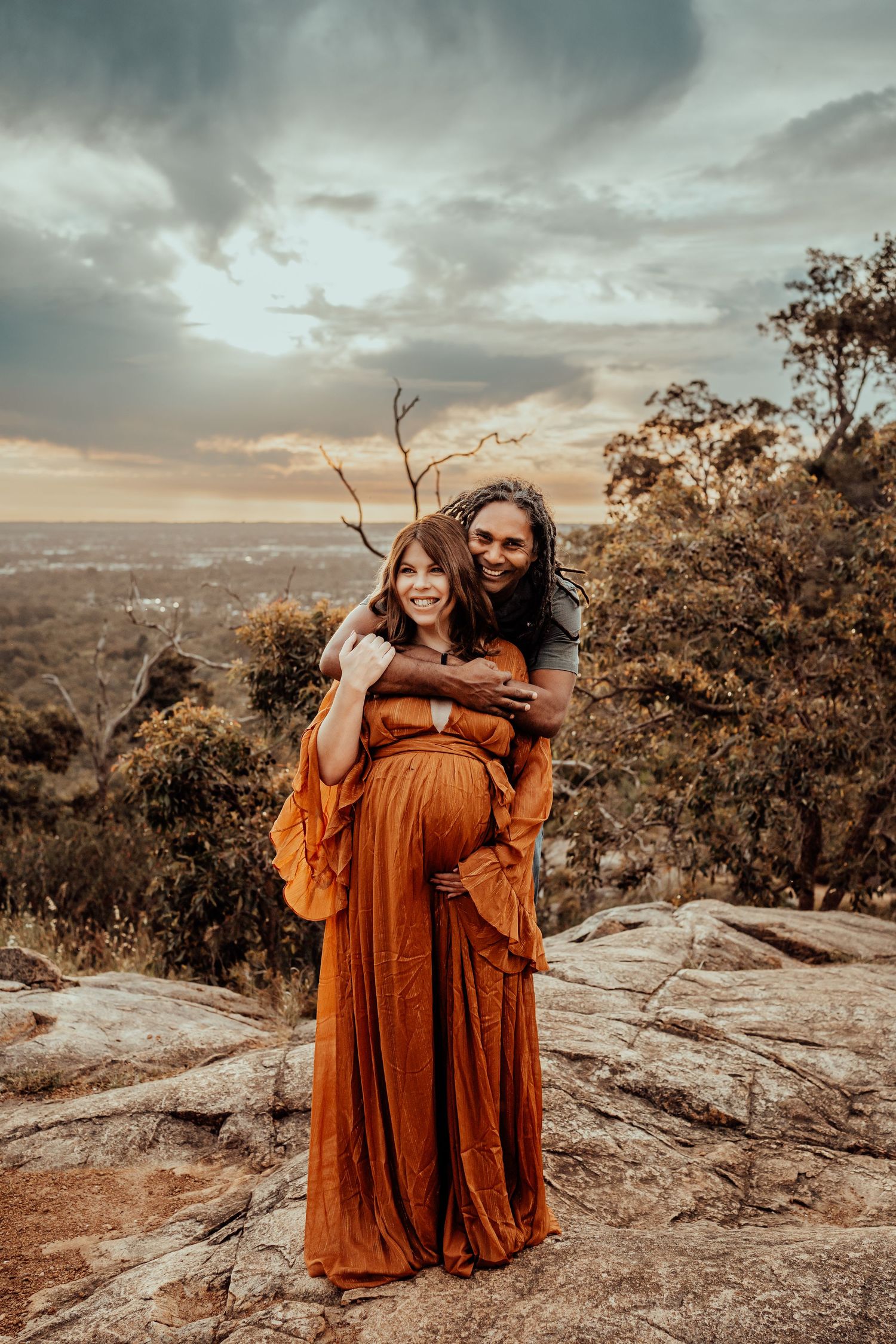 Intimate maternity photo with couple embracing on scenic mountain overlook.