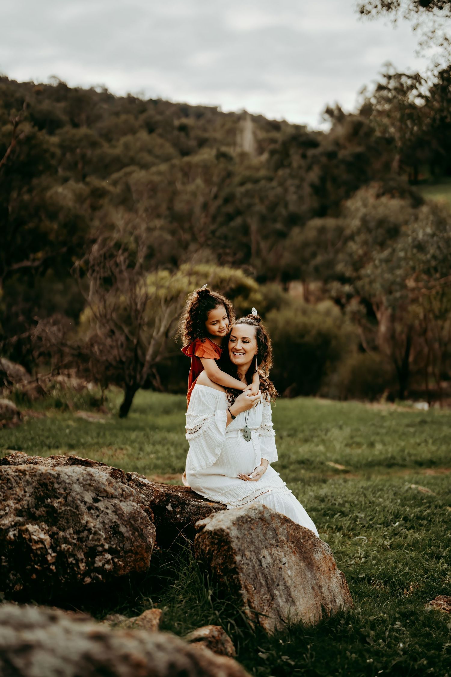 Mother and daughter posing playfully on large rocks in a natural bush setting.