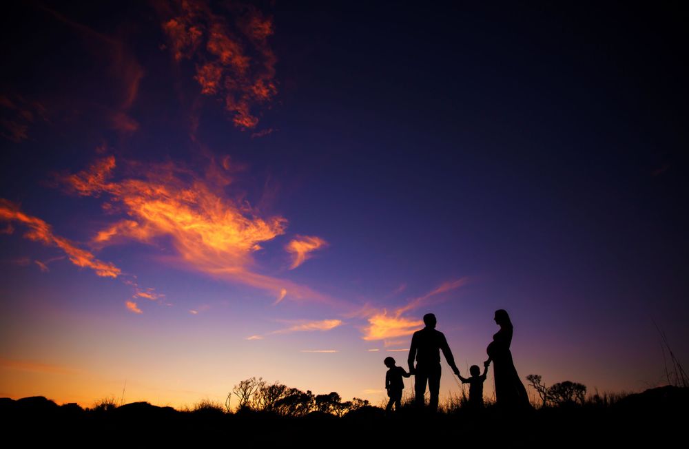 Silhouettes of a family holding hands against a vibrant sunset sky with purple and orange clouds.
