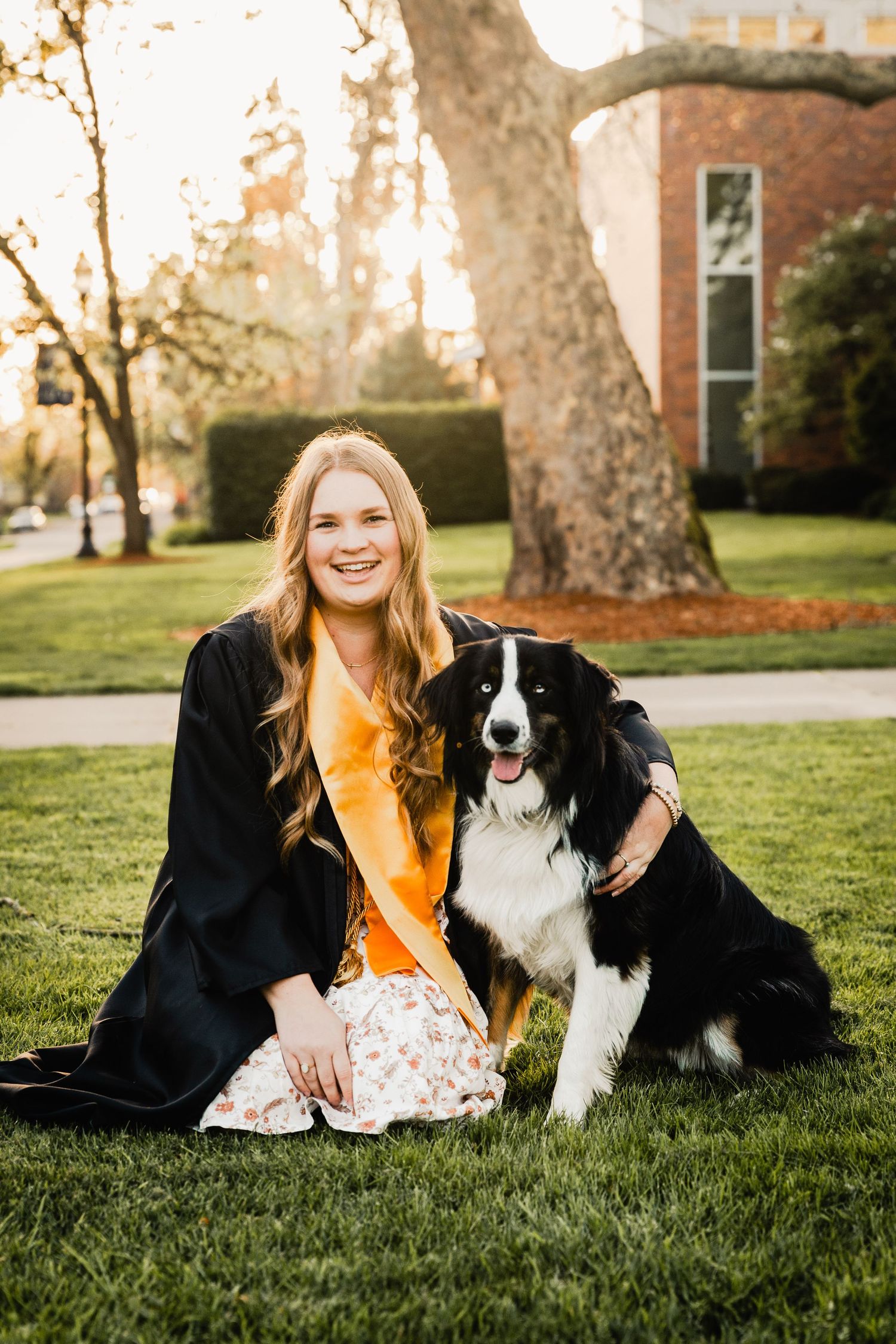 Happy woman in yellow top sitting on grass with friendly Border Collie dog.