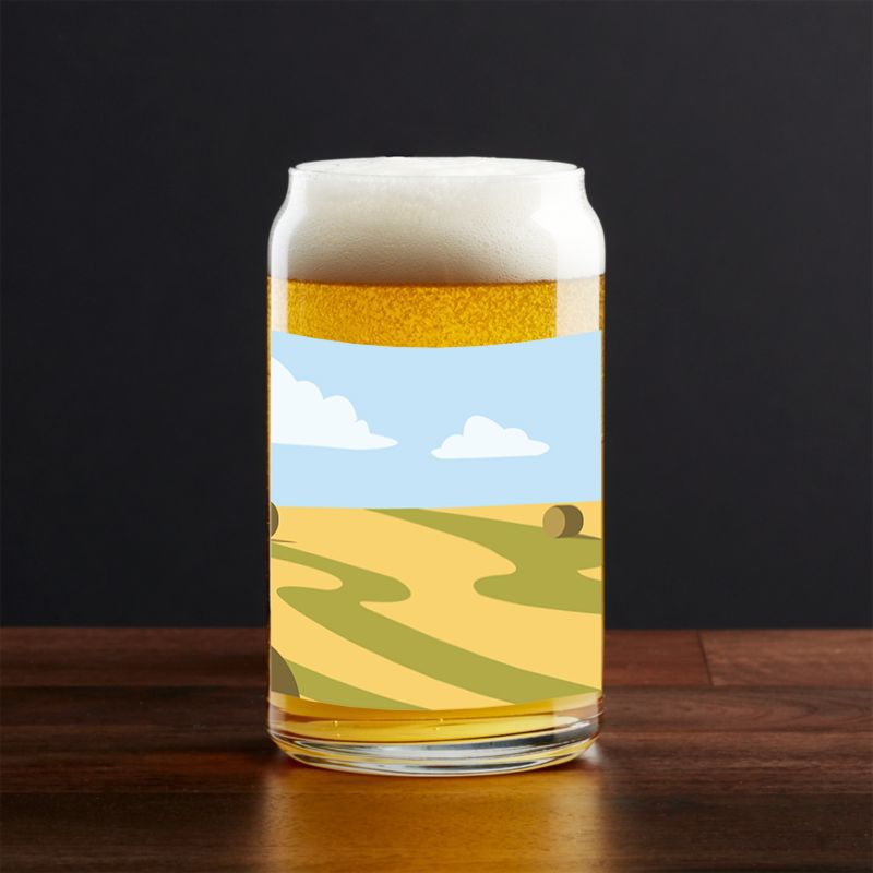Beer glass featuring pastoral farm scene artwork on wooden surface.