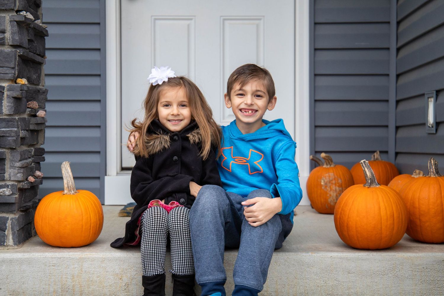 Children sitting on porch steps with orange pumpkins during autumn season.