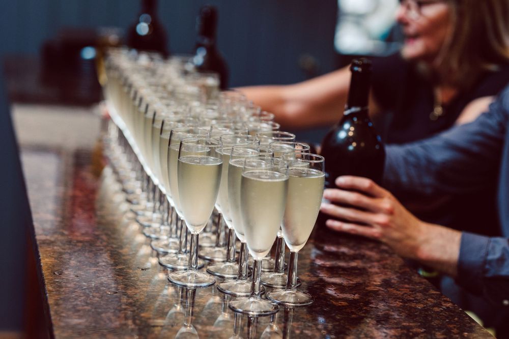 Row of champagne glasses lined up on a dark wooden bar surface.