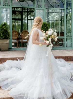 A flowing white wedding dress with a dramatic tulle train photographed in front of an ornate mint green conservatory.