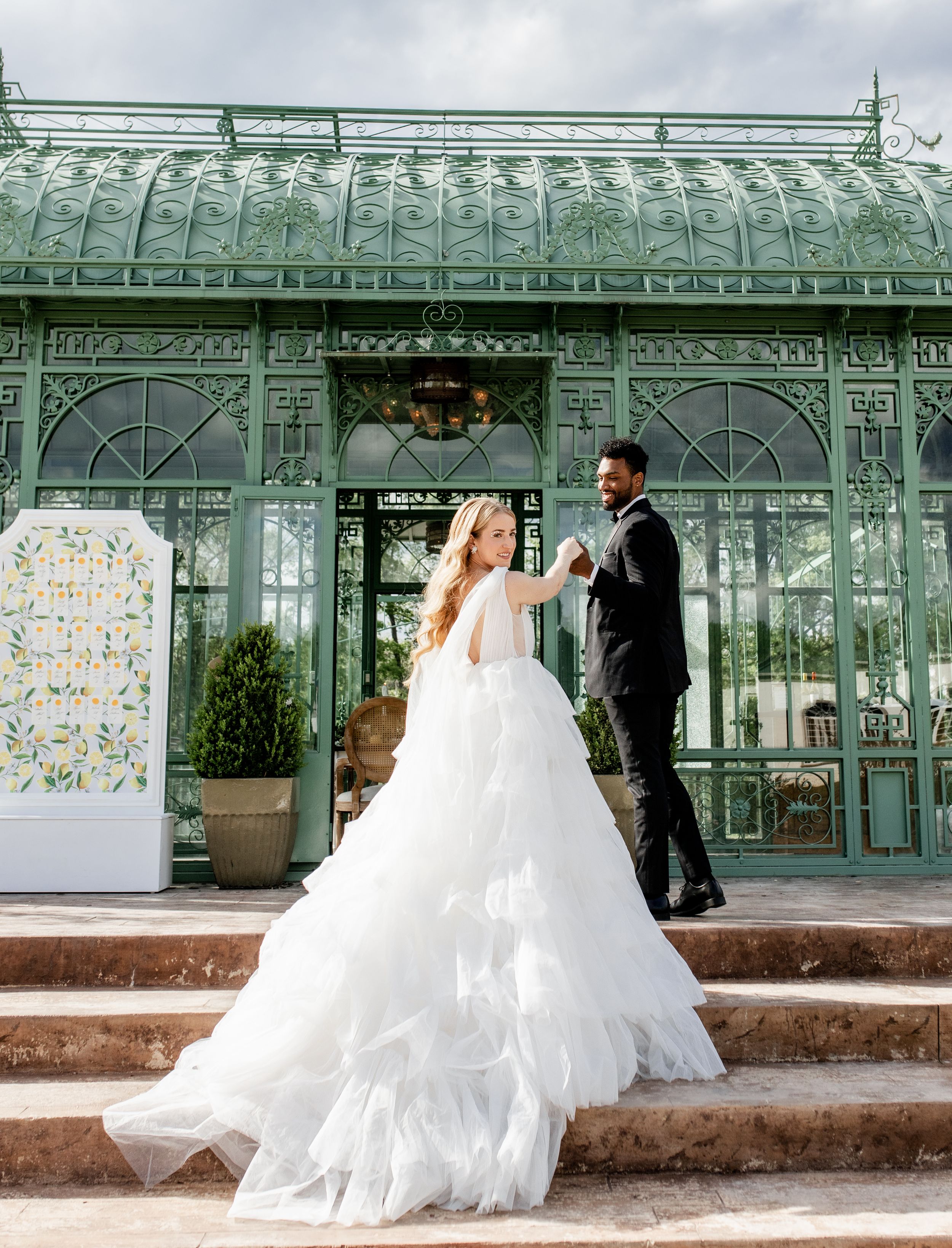 Wedding couple ascending stairs in front of a vintage mint green conservatory building.
