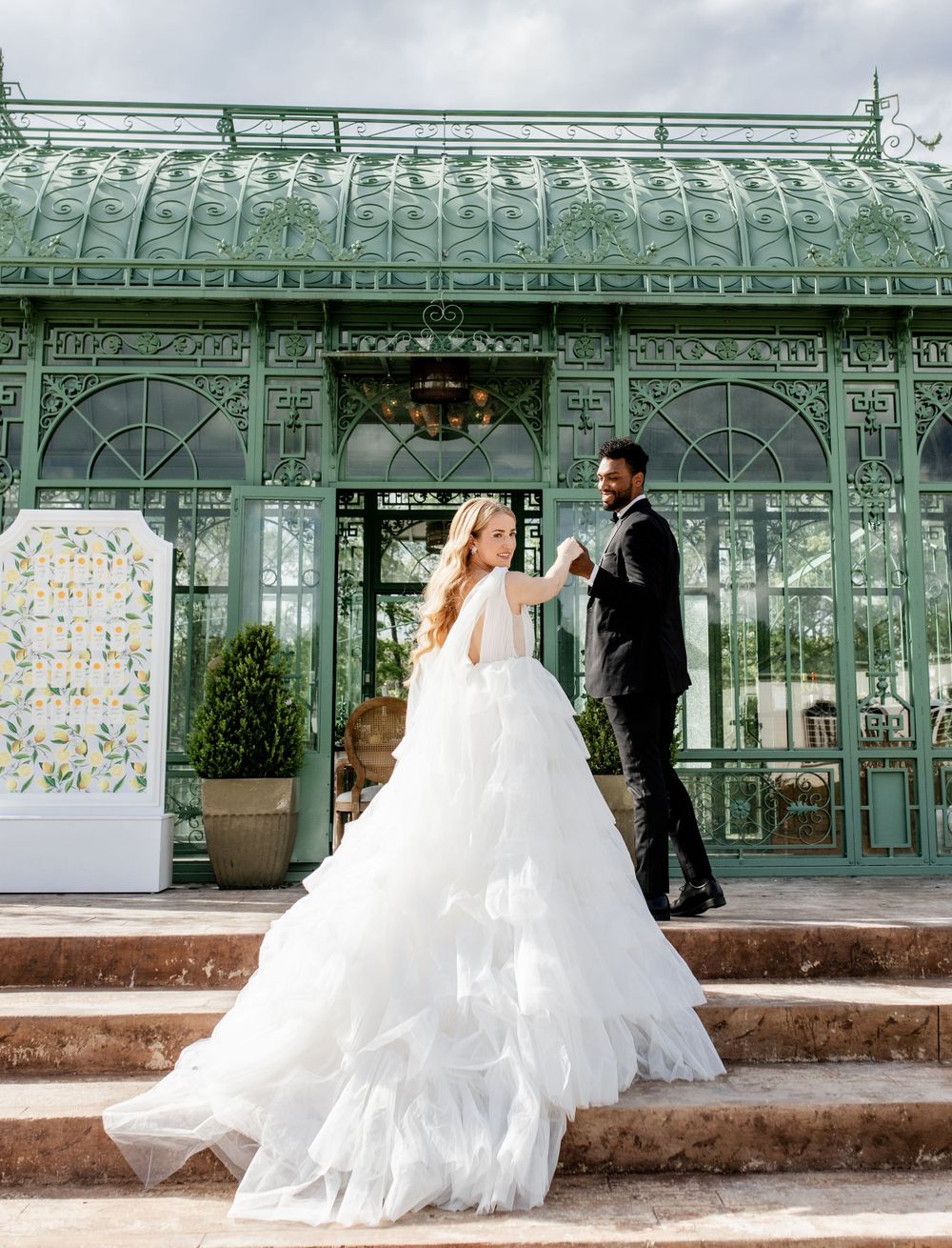 Wedding couple ascending stairs in front of a vintage mint green conservatory building.