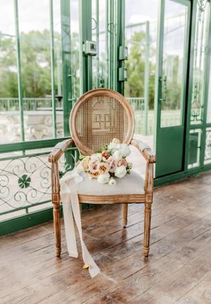 An elegant vintage cane chair with floral bouquet arrangement against green glass doors.