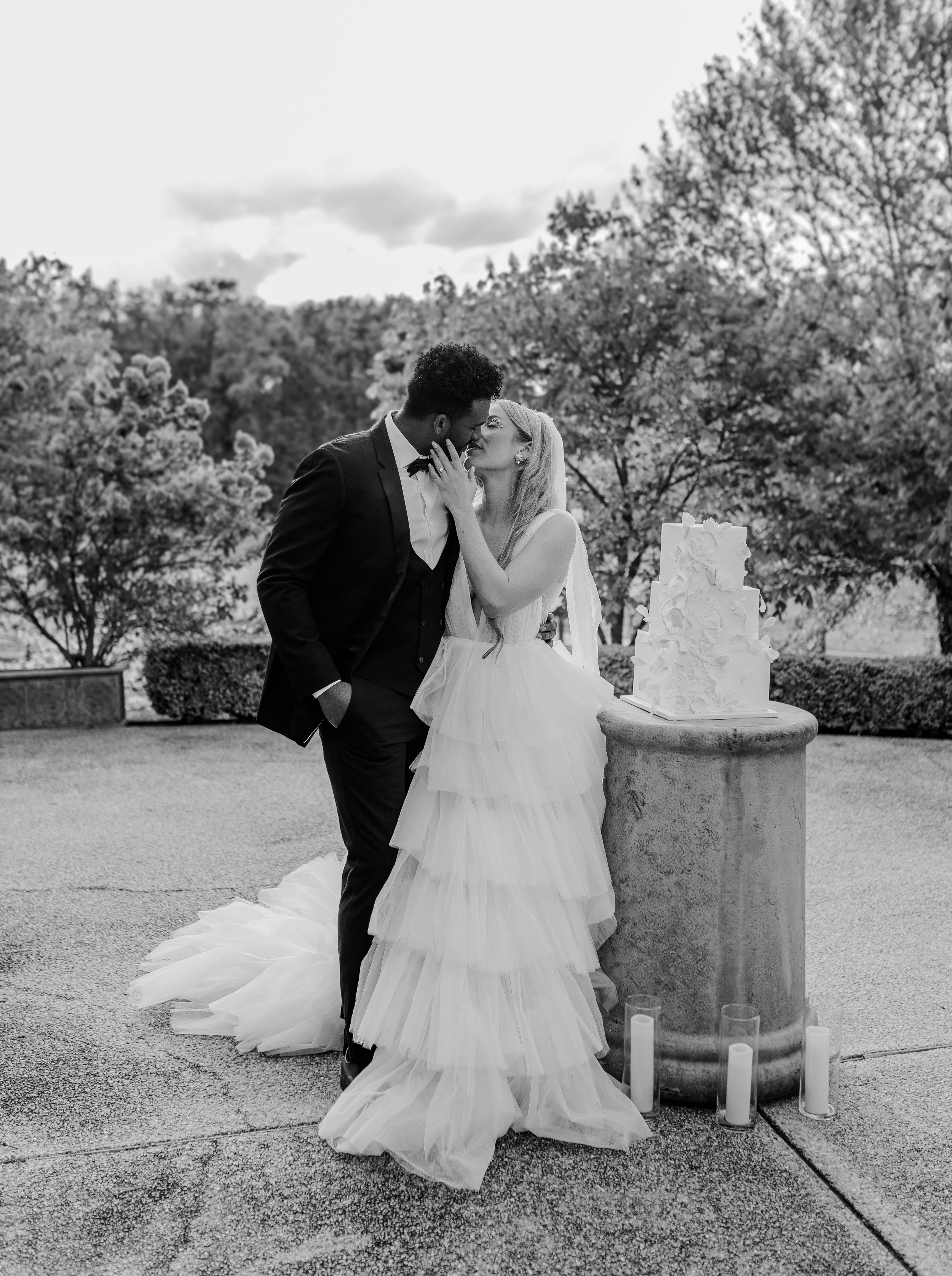 Black and white wedding portrait with tiered dress next to a decorative stone pillar.