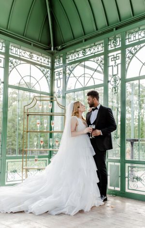 Elegant wedding portrait in a Victorian-style green conservatory with ornate architectural details.