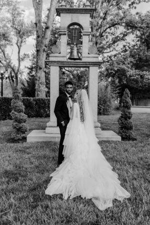 Black and white wedding portrait with dramatic train by stone bell tower.